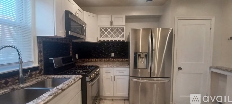 A kitchen with a stainless steel refrigerator and black countertops.