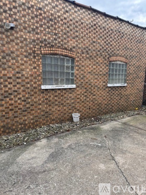 A brick building with two windows and a white bucket on the ground.