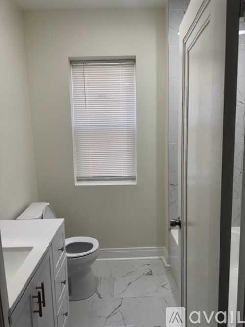 A bathroom with a toilet, sink, and a window with blinds.