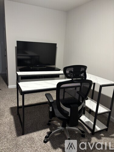 A black office chair is in front of a desk with a television on it.