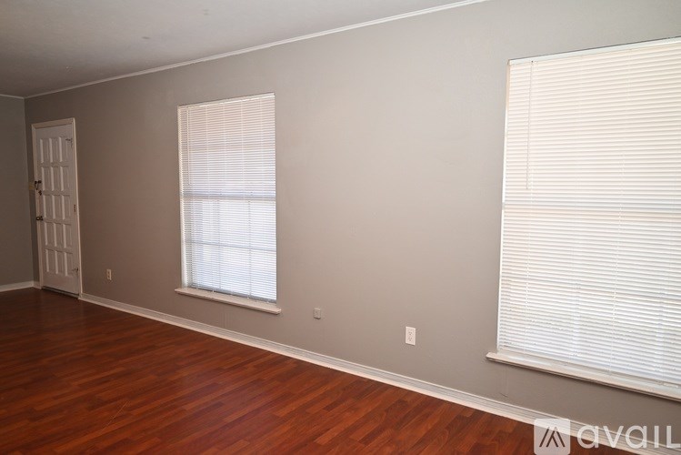 A room with wooden floors and two windows with blinds.