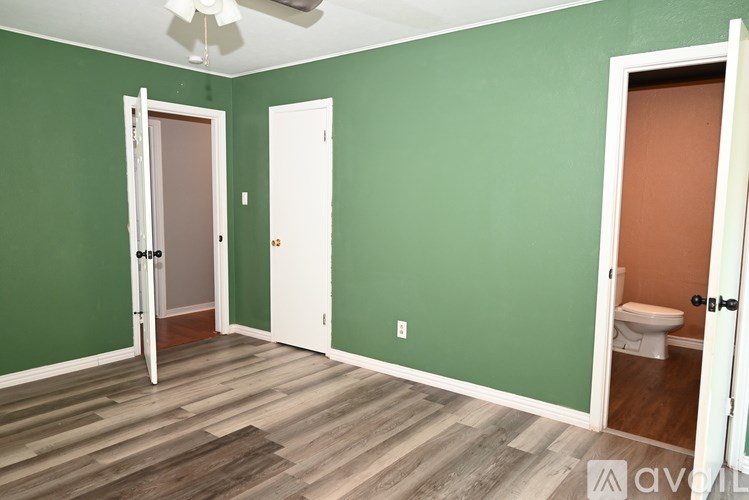 A room with green walls and wood flooring with a ceiling fan.