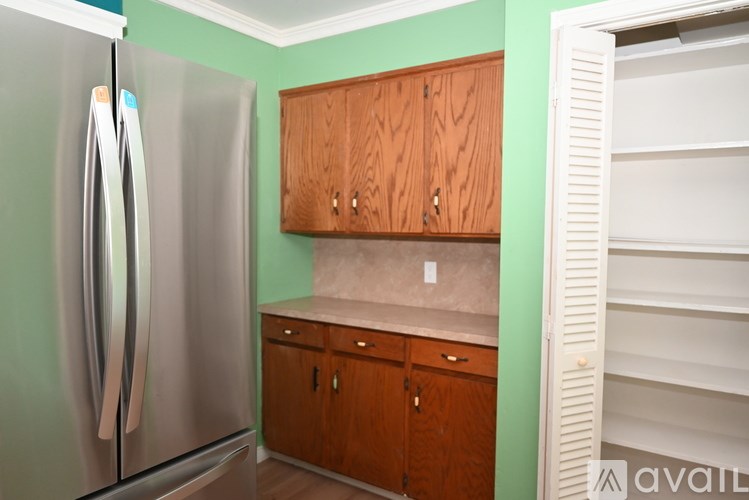 A kitchen with a refrigerator, wooden cabinets, and a white shelf unit.