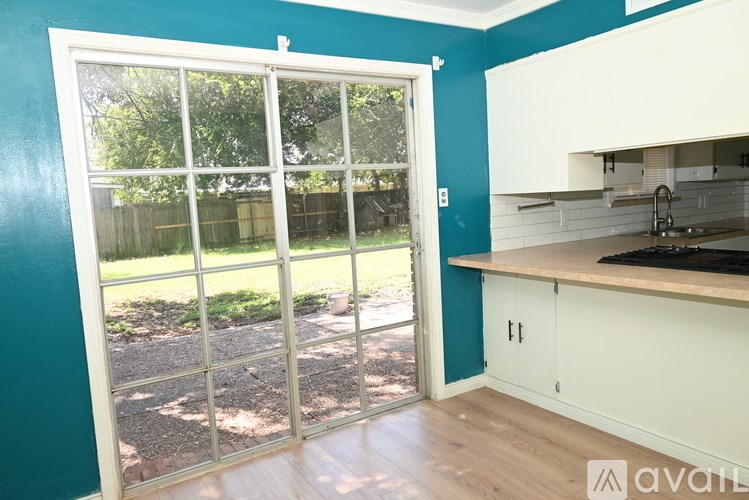 A kitchen with a white counter and cabinets with a blue wall and a sliding glass door.