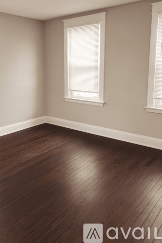 A room with wooden flooring and two windows.