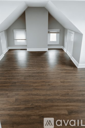 A spacious attic room with wooden flooring and white walls.