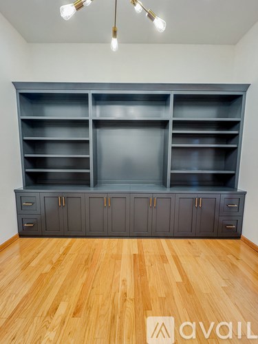 A large grey shelving unit with doors and drawers is in a room with wooden flooring and white walls.