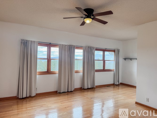 A room with a ceiling fan and large windows with curtains.