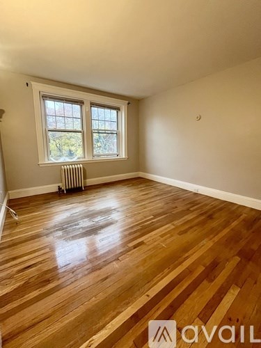 A room with wooden flooring and a window with a radiator beneath it.