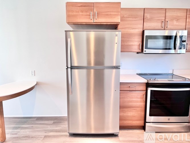 A stainless steel refrigerator stands in a kitchen with wooden cabinets and a microwave above it.
