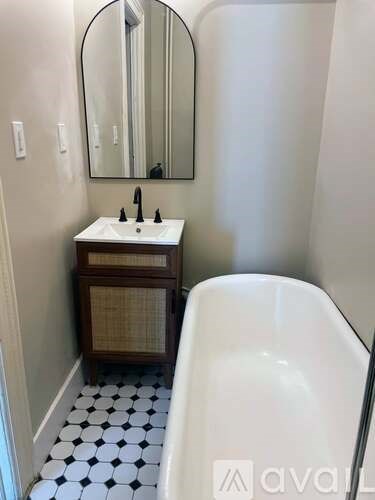 A white sink with a black faucet is on a counter next to a mirror.