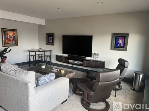 A living room with a grey couch, a black chair, a black coffee table, a flat screen TV, and a couple of pictures on the wall.