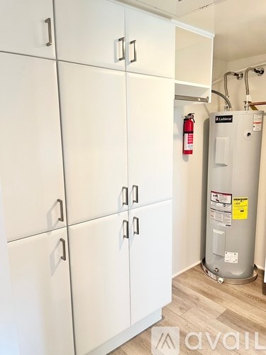 A row of white cupboards with a water heater and fire extinguisher behind them.