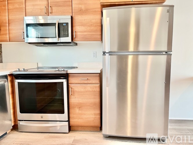 A stainless steel refrigerator stands next to a microwave and oven in a kitchen.