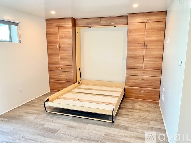 A bedroom with a bed, wooden cabinets, and a window.