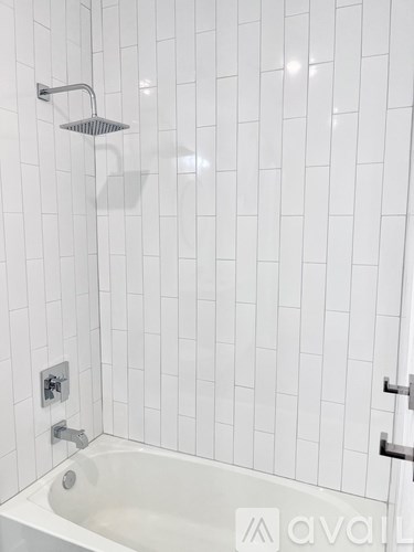A white tiled shower with a white bathtub and a silver shower head.