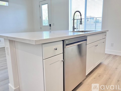 A white kitchen with a stainless steel dishwasher and a white countertop.