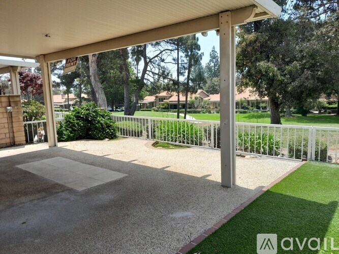 A patio area with a white fence and a grassy area in the background.