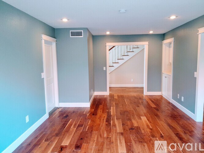 A room with wooden floors and a staircase in the background.