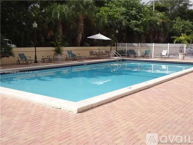 A pool surrounded by a brick patio and a white fence.
