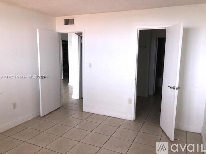 A room with white walls and tile flooring, with two doors open.