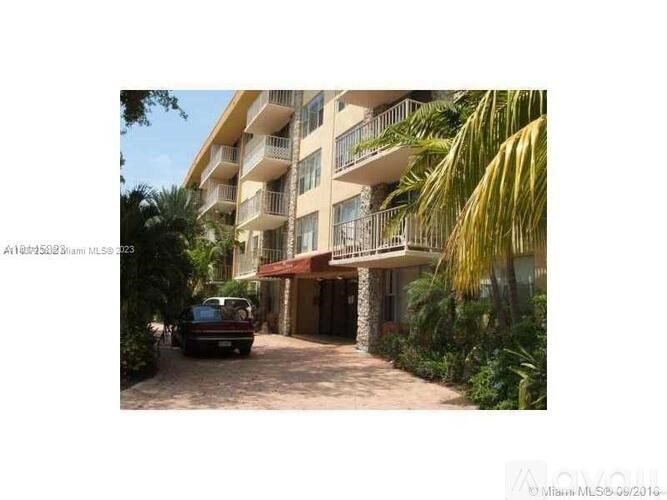 A car is parked in front of a building with balconies and surrounded by greenery.