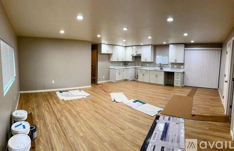 A room with wooden flooring and a kitchen area in the background.