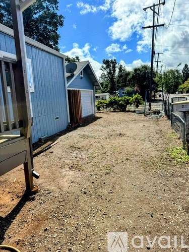 A backyard with a blue house and a dirt ground.