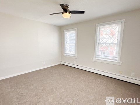 A room with a ceiling fan and two windows.