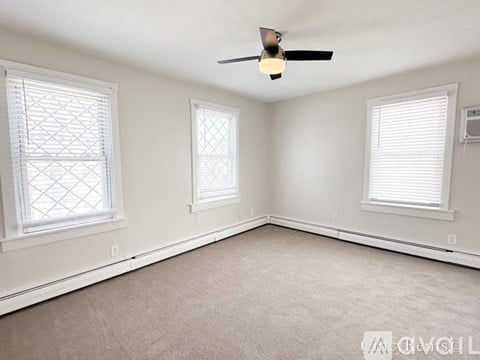 A room with a ceiling fan and two windows.