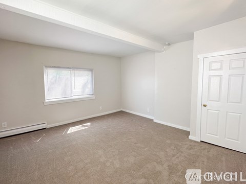 A room with a white door, carpeted floor, and a window with blinds.