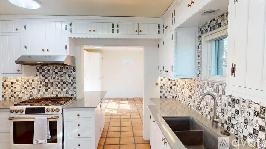 A kitchen with white cabinets and a black and white tiled backsplash.