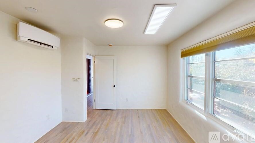 A room with a wooden floor and a window overlooking a tree-filled area.
