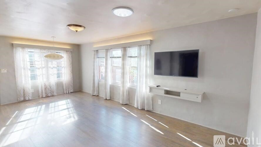 A spacious living room with a television and a window with curtains.