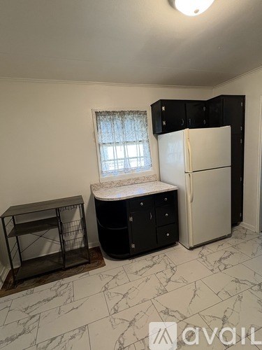 A kitchen with a white fridge, black cabinets, and a marble floor.