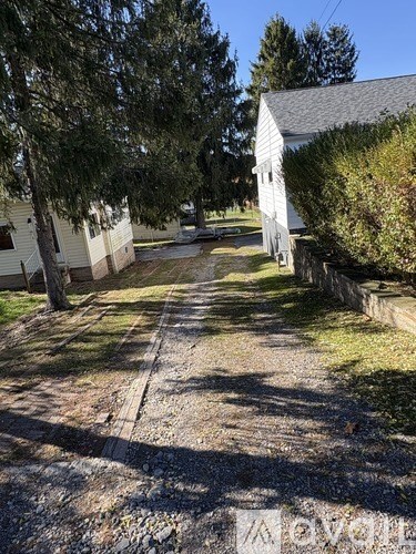 A gravel road leads to a white house with a grey roof.