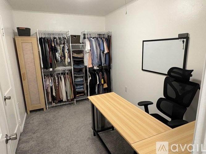A room with a desk, chair, and a closet full of clothes.