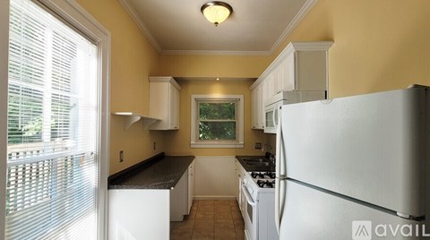A kitchen with white appliances and a window with blinds.