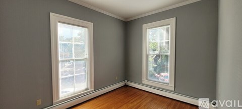A room with two windows and wooden floors.