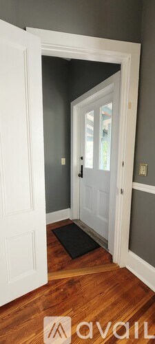 A white door is open to a hallway with a black mat on the floor.