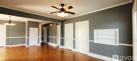 A large empty room with a ceiling fan and wooden floors.