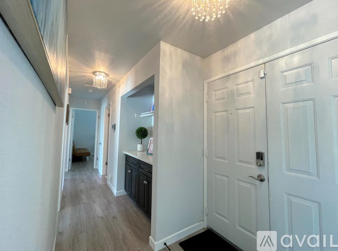 A hallway with a white door and a chandelier hanging from the ceiling.