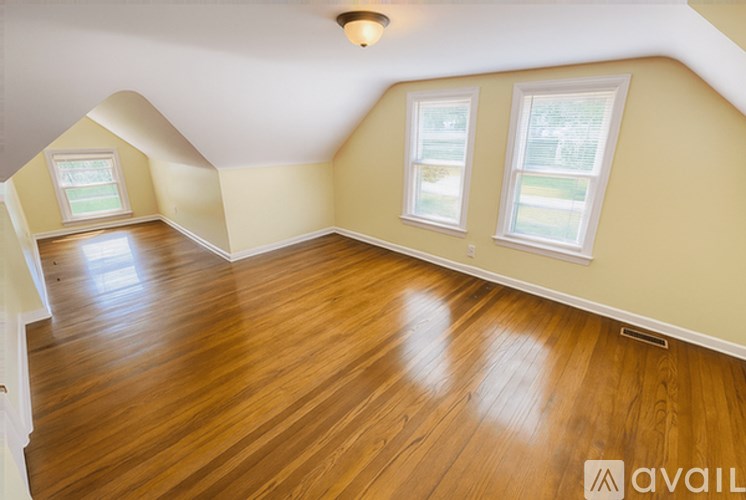 A room with wooden flooring and two windows.