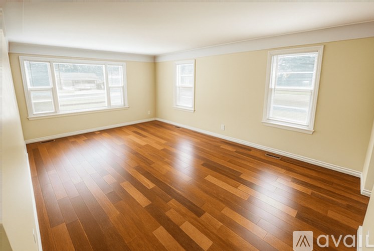 A room with wooden flooring and two windows.