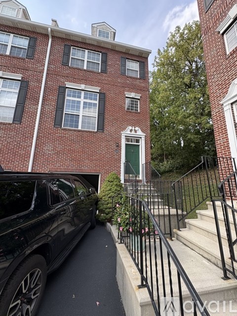 A black car is parked on a driveway in front of a red brick building.
