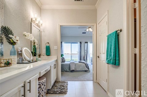 A well-lit, spacious bathroom with a vanity, mirror, and a view of a bedroom through the open door.