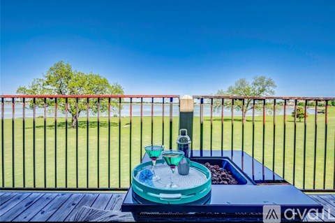 A glass of water is placed on a table with a view of a green lawn and trees.