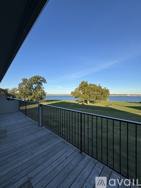 A deck overlooking a grassy field with trees and a body of water.