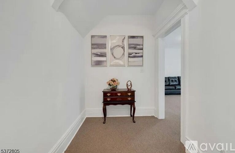 A room with a brown carpet and a wooden table with a vase of flowers on it.