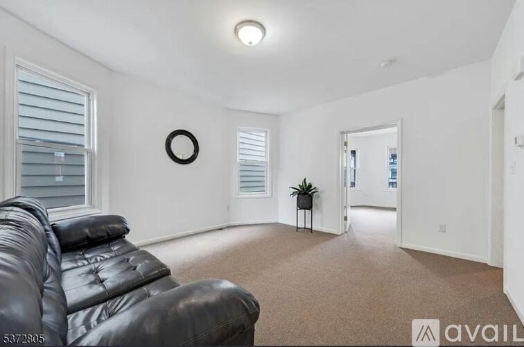 A black leather couch sits in a brightly lit room with a white wall and a small plant on a stand.
